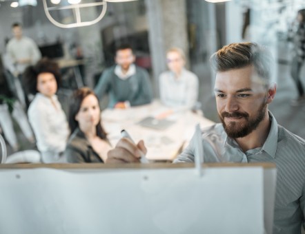 Mann schreibt vor einem Team mit vier Personen etwas an ein Whiteboard